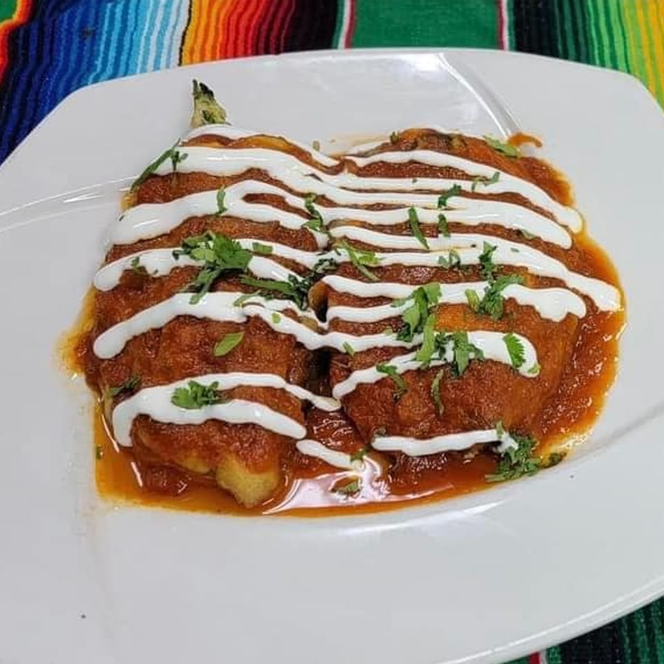 Two chili rellenos covered in red sauce, white crema, and fresh cilantro on a white plate.