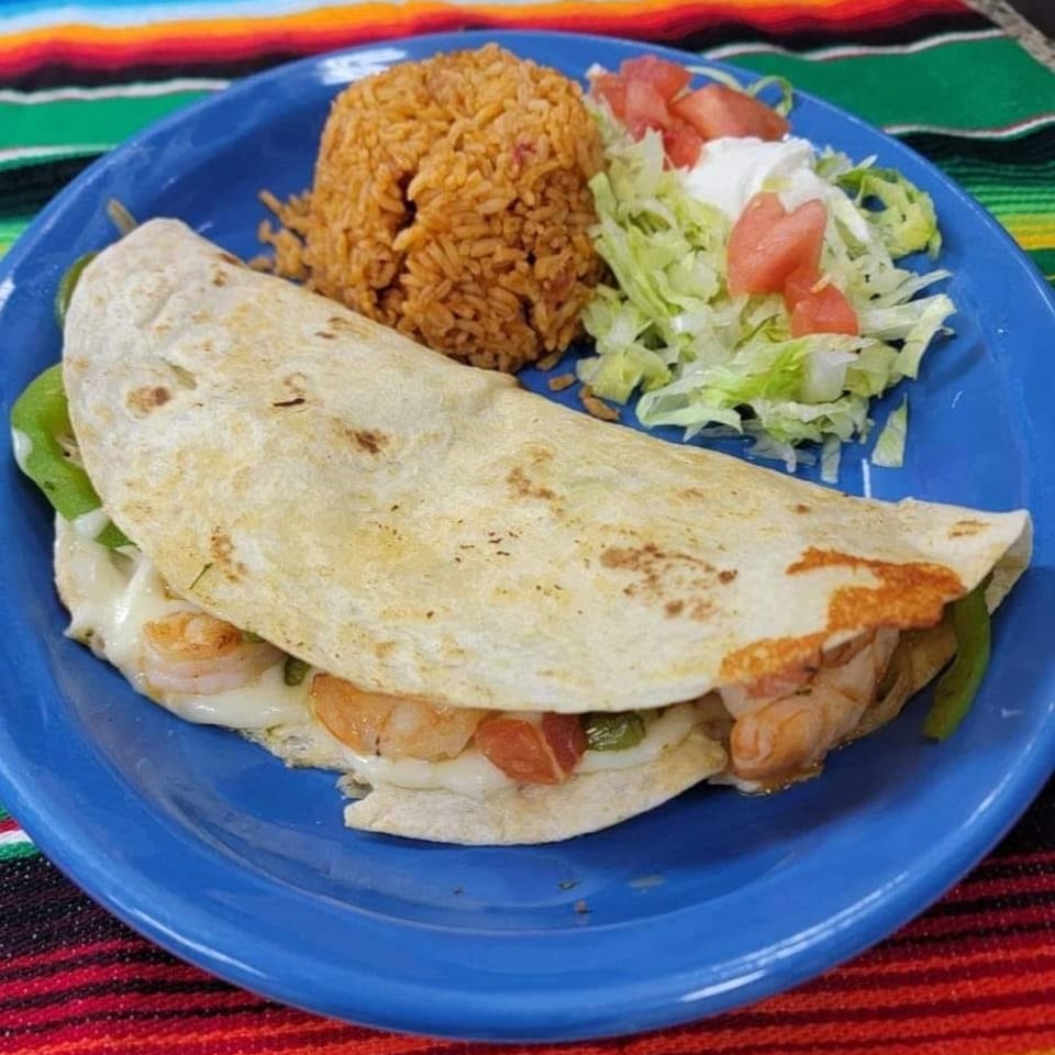A shrimp quesadilla with melted cheese, green peppers, rice, and a side salad on a blue plate.