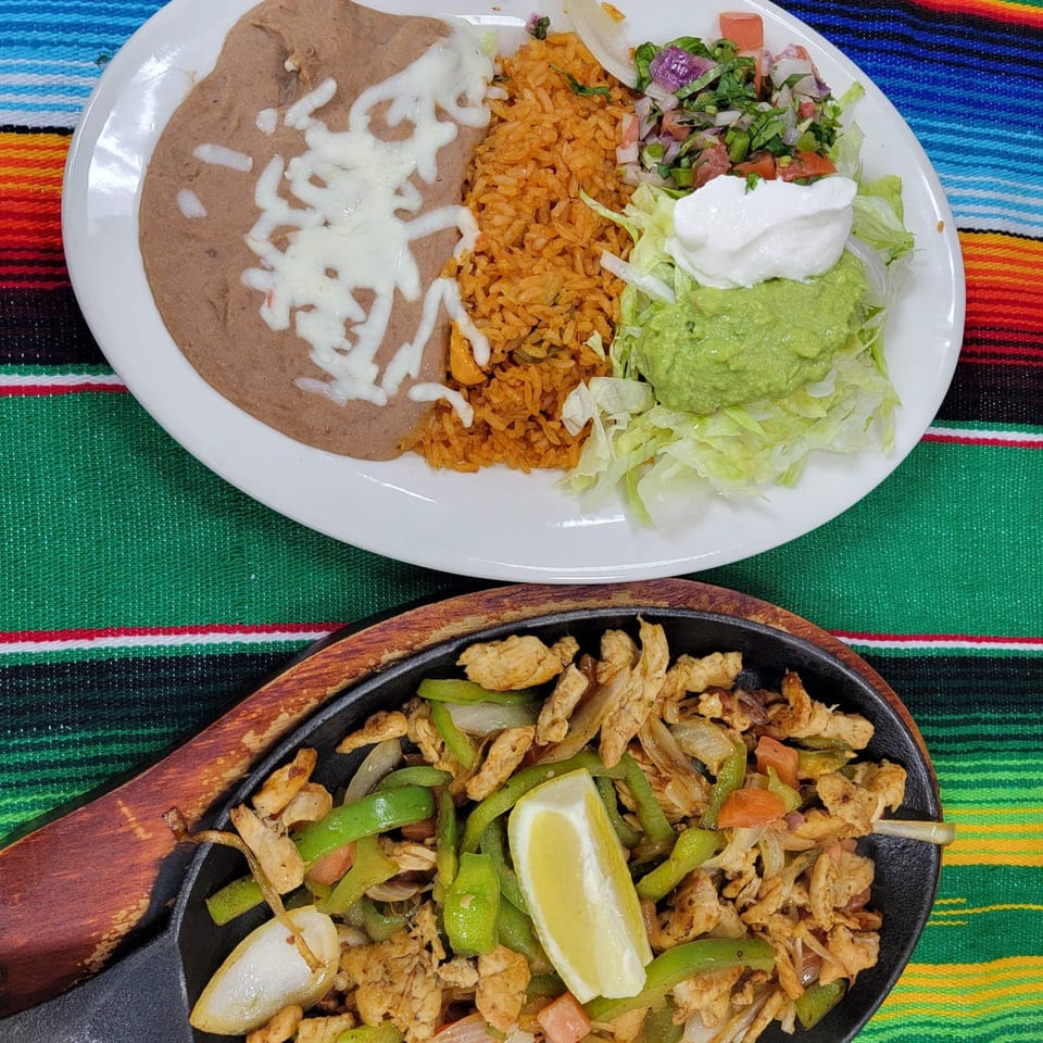 Mexican fajitas with chicken, peppers, and onions, alongside a plate of rice, beans, and guacamole.